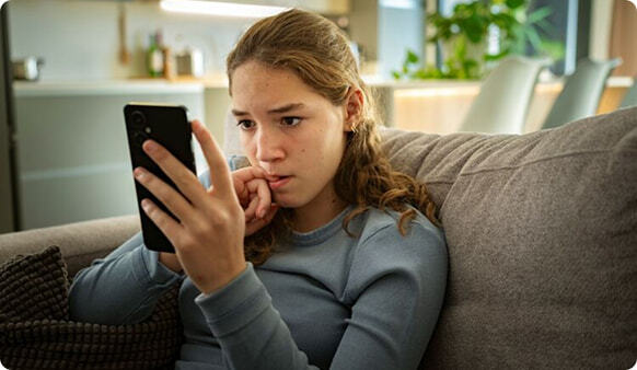 Portrait of nervous teen girl looking at smartphone biting nails worried about bullying